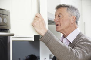 An older man peers into a cabinet with a confused look on his face, a common occurrence when someone with dementia is hiding things.