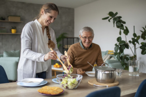 A caregiver who knows how to help older adults eat healthy tosses a salad for an older man.