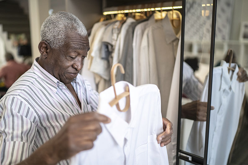 An older man considers whether to put on a clean shirt or to resist changing clothes.