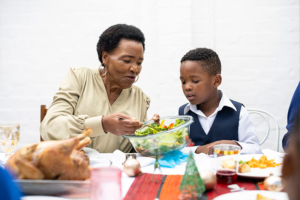 An older woman hands a plate of holiday food to her grandson as she implements holiday blood pressure management tips for herself.