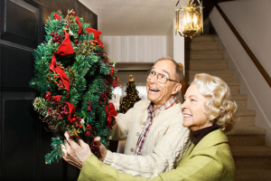 An older man and his wife hang a wreath on their front door, showcasing the joy of holiday traditions for seniors with dementia.