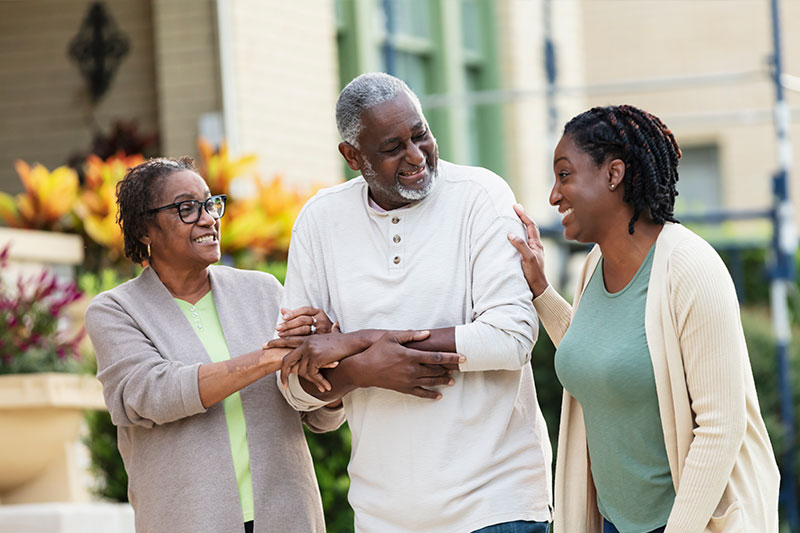 A woman managing care for two parents smiles as she goes out for a walk with them.