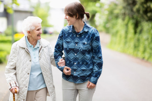 A woman works on preventing senior falls by linking arms with her older mother as they go for a walk.