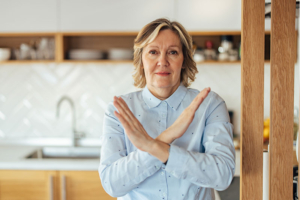 A woman who understands pushing yourself beyond your limits as a caregiver makes an X with her arms to symbolize saying no and setting healthy boundaries.