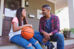 A man who knows how to respond when your child has questions about dementia listens carefully to his daughter as they sit together on the porch.